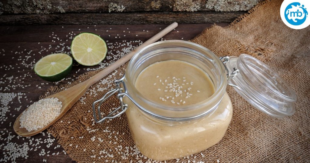 fresh sesame paste in a mason jar with a wooden spoon, lemon slices, and wooden background
