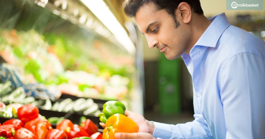 a young Indian man in a blue shirt, buying red and yellow bell peppers from a vegetable store