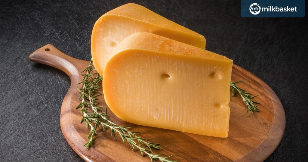 A thick Slice of Gouda cheese on a wooden chopping board decorated with rosemary  
