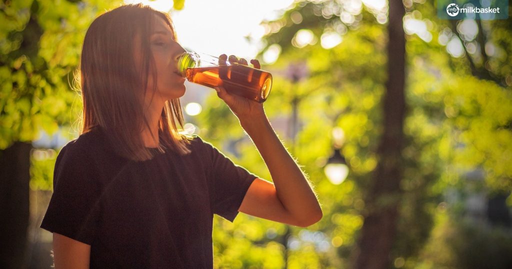 woman are drinking iced tea after workout exercising on sunset evening in park