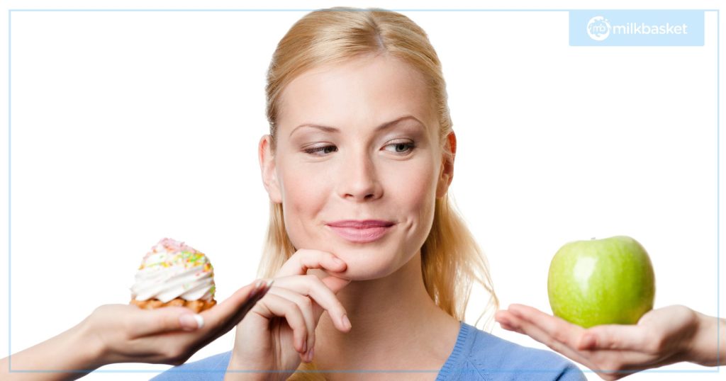 A woman choosing between a cupcake and an apple