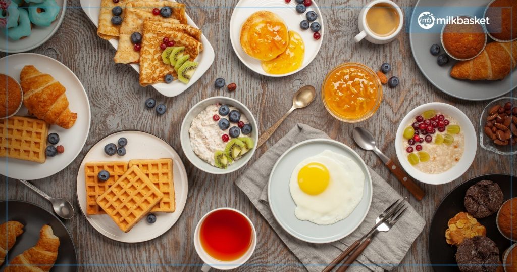 Various breakfast items such as pancakes, waffles, jam and croissants kept in white plates on a wooden table 
