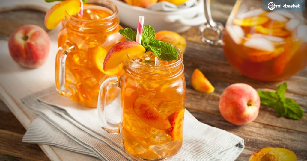 Mason Jar filled with fresh peach iced tea with whole peaches kept at the side on a kitchen towel.