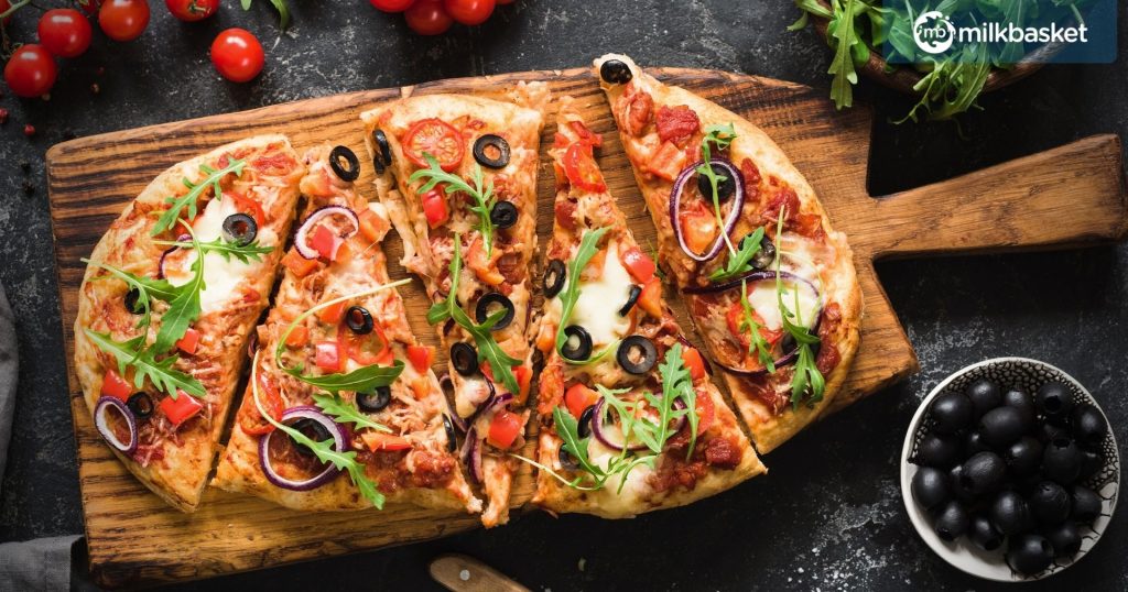  Flatbread pizza garnished with fresh arugula on wooden pizza board, top view. Dark stone background