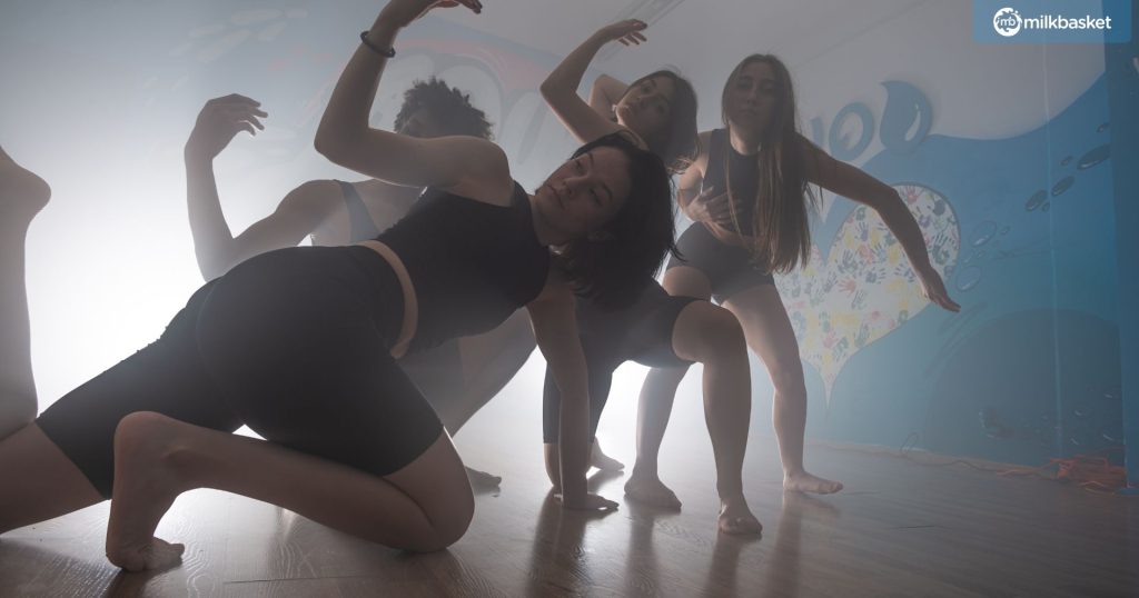 a group of dancers in black workout clothes, performing flexible dance movements.