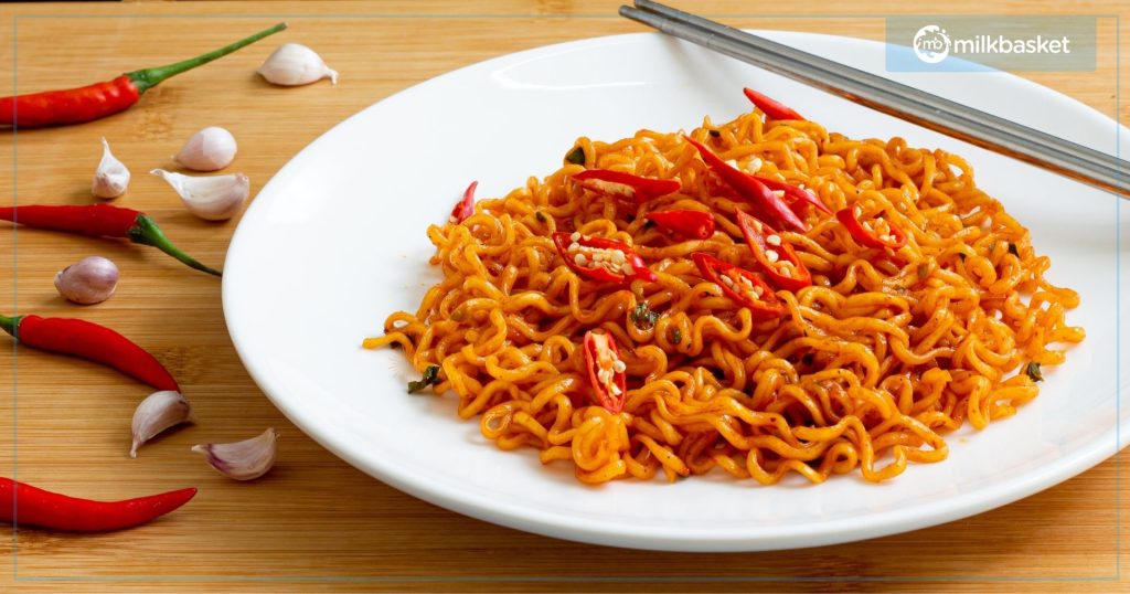 white plate with spicy red noodles, garnished with chopped red chillis