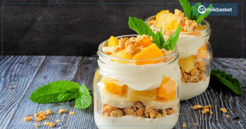 Yogurt and Granola parfait in a jar with mint leaves and chopped mango