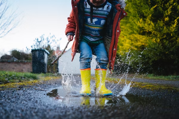 Kid in bright yellow rain boots playing in a water puddle.