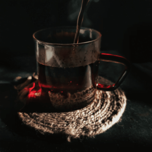 A glass cup filled with rich, dark black tea, sitting on a rustic coaster, showcasing the robust and full-bodied nature of this popular type of tea.