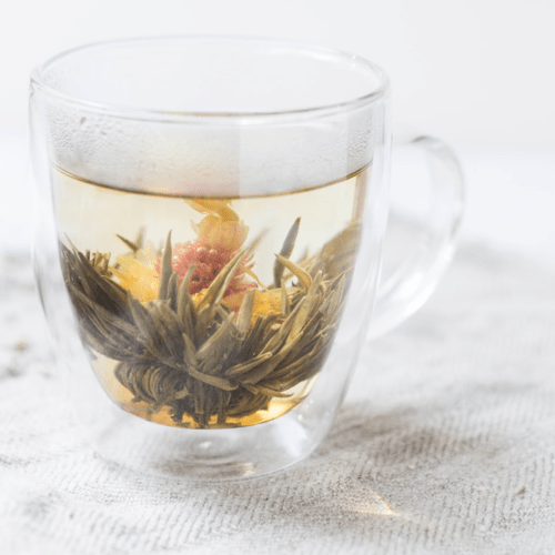 A transparent cup of flower tea with a blooming tea flower inside, illustrating the delicate and aromatic experience of this unique type of tea.