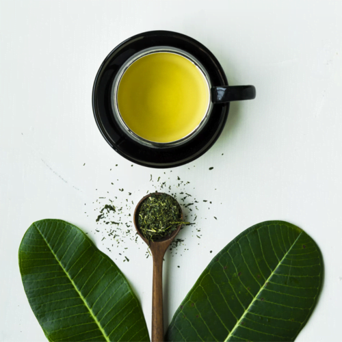 A black cup of green tea with tea leaves and green leaves arranged around it, highlighting the fresh and grassy notes of this popular type of tea.