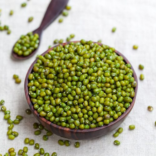 A bowl of vibrant green moong dal beans, perfect for healthy dal recipes, sitting on a light fabric with a wooden spoon beside it.