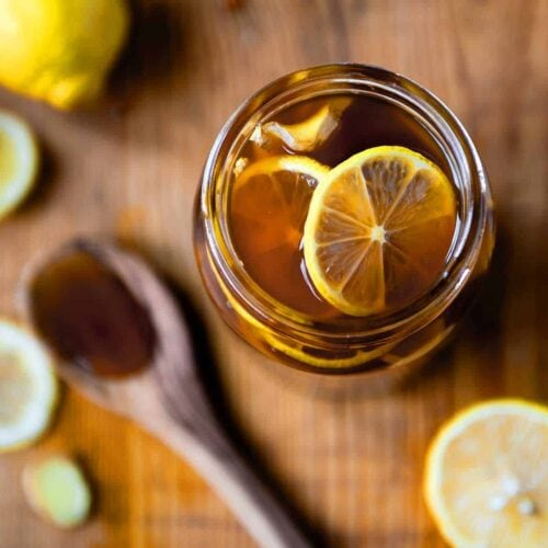 A jar filled with lemon slices immersed in honey, alongside a wooden spoon with honey on a wooden surface.