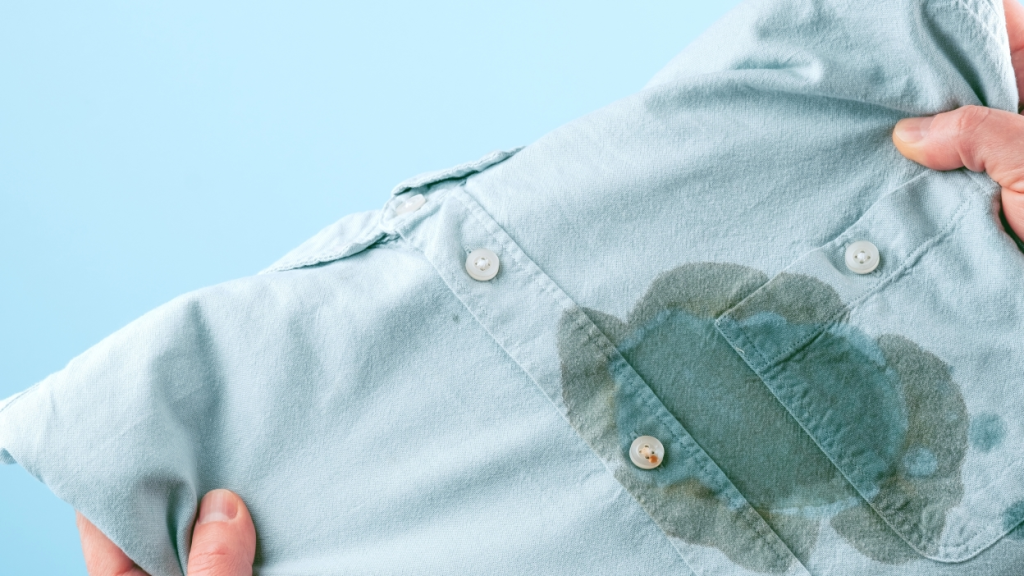 A close-up of a light blue shirt with a large, dark oil stain on the front, showing a common tough stain problem on clothing.