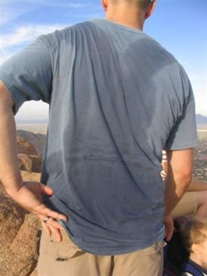 A man with visible sweat stains on the back of his blue t-shirt, showing the difficult-to-remove stains caused by perspiration.