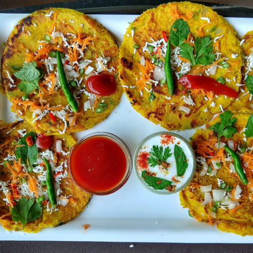 A plate of golden-brown paneer besan cheelas garnished with fresh vegetables and served with chutney and yogurt, highlighting a protein-packed and healthy breakfast option.