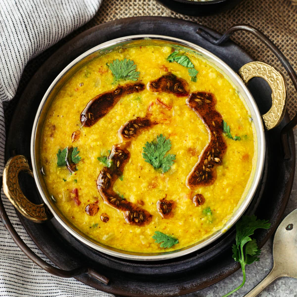 A beautifully prepared bowl of moong dal, garnished with fresh coriander leaves and drizzled with a rich, aromatic tempering of spices. 