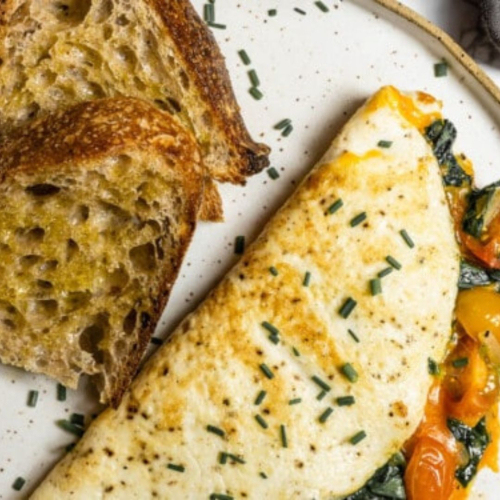 A plate featuring a fluffy egg whites omelette garnished with herbs, served with two slices of toasted whole wheat bread, highlighting a protein-rich healthy breakfast option.