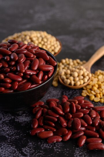 A bowl filled with red beans, surrounded by scattered beans and a spoonful of lentils in the background, showcasing rich protein sources for vegans