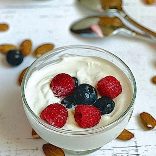 A glass bowl of Greek yogurt topped with fresh blueberries and raspberries, a nutritious vegetarian protein source